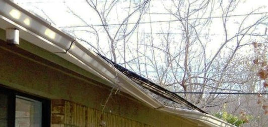 Residential gutter and roof edge near bare branches on a home exterior